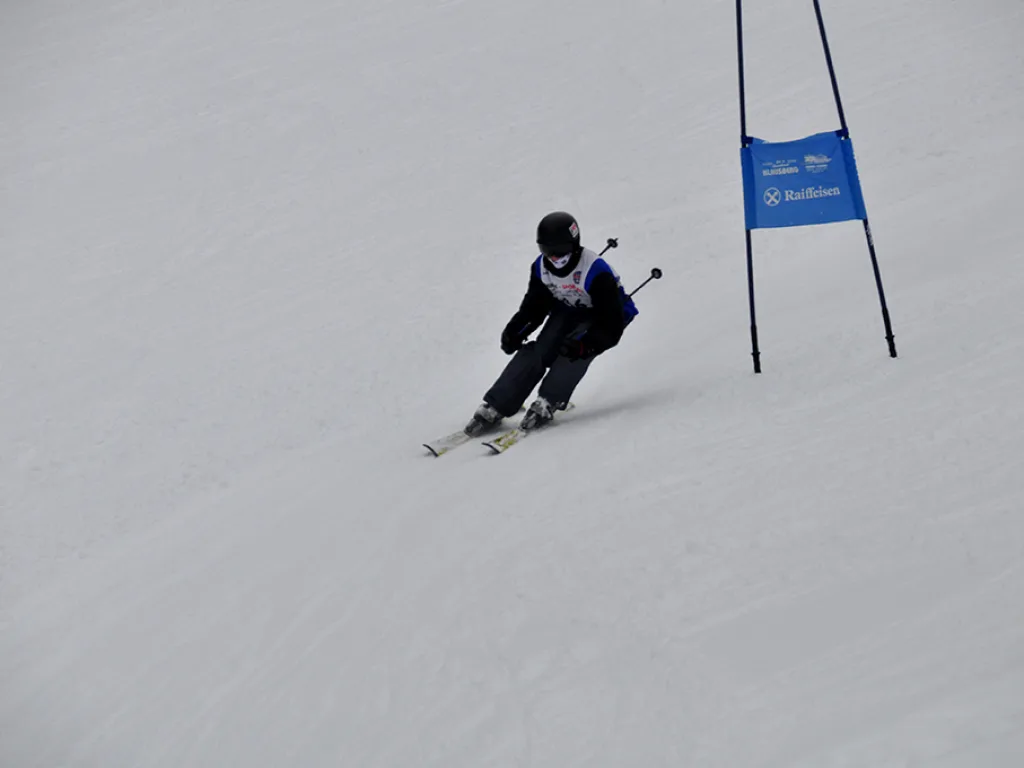 Skifahrer in tiefer Hocke neben dem blauen Tor.